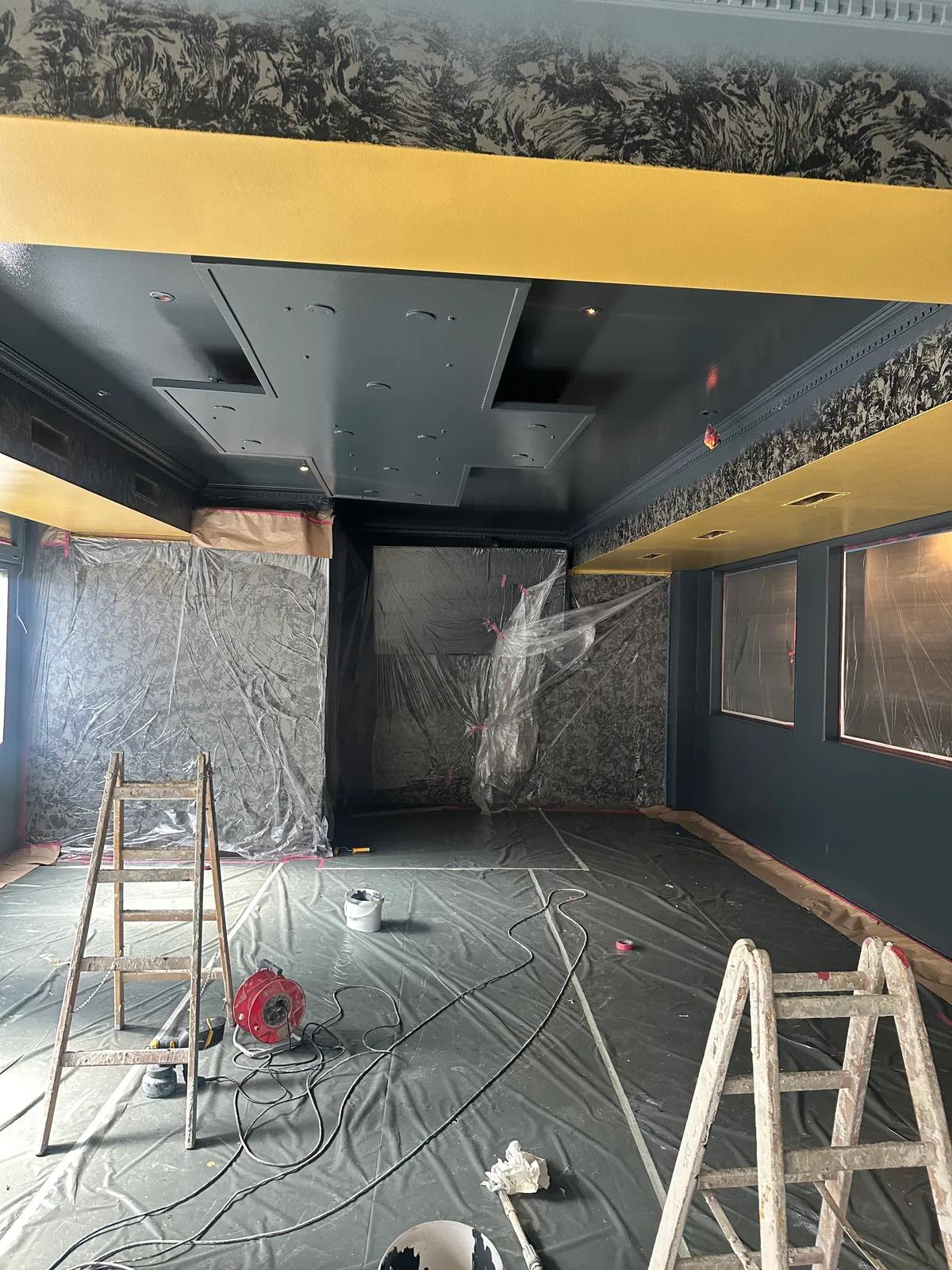 Salle en travaux : échelles, protections au sol et surfaces en cours de reprise
